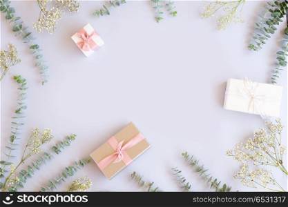 Gift boxes with green leaves. Green eucaliptus leaves with gift boxes on blue table from above with copy space, flat lay frame