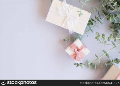 Gift boxes with green leaves. Green fresh leaves with gift boxes on blue table from above with copy space, flat lay scene