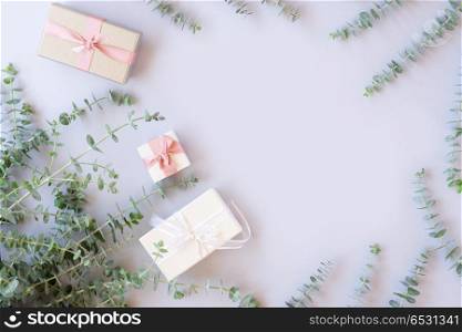Gift boxes with green leaves. Green fresh leaves with gift boxes on blue table from above with copy space, flat lay scene
