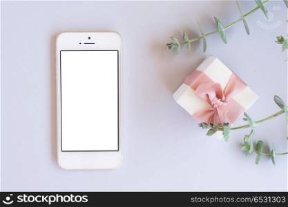 Gift boxes with green leaves. Green leaves with gift box and modern phone on blue table with copy space, flat lay top view scene