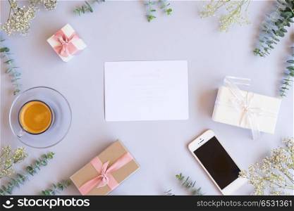 Gift boxes with green leaves. Green leaves with gift boxes, mobile phone and coffee on blue table from above with copy space on paper note , flat lay scene