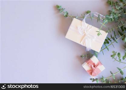 Gift boxes with green leaves. Green leaves with gift boxes on blue table from above with copy space, flat lay scene