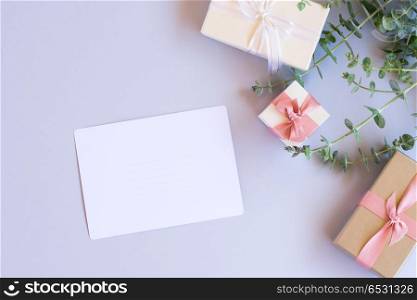 Gift boxes with green leaves. Green leaves with gift boxes on blue background from above with copy space on paper note, flat lay scene