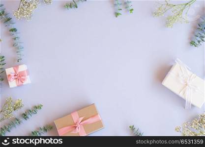 Gift boxes with green leaves. Green leaves with present gift boxes on blue table from above with copy space, flat lay frame