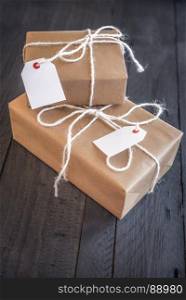 Gift boxes, wrapped with brown paper and white flax rope, having tags attached with space for your text, on an old wooden table.
