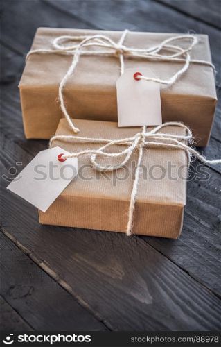 Gift boxes wrapped with white flax string and vintage brown paper, with blank labels attached, displayed on an old wooden table.