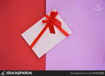 Gift card on red and pink background / Gift card decorated with red ribbon bow to Merry Christmas Holiday Happy new year or Valentines day Gift voucher on red half pink background top view
