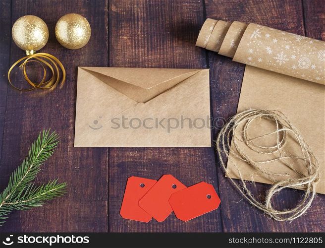 Gift envelope for Santa letter from handmade craft paper on a wooden background in the New Year s style, decorated with Christmas balls, cones, a ball of rope, spruce branches. Christmas, New Year, winter holiday. Kraft package, holiday concept, top view, flat lay. Mocap.. Gift envelope for writing from handmade kraft paper on a wooden background in the New Year style, decorated with balls, cones, a ball of rope, spruce branches. Christmas, New Year, winter holiday.