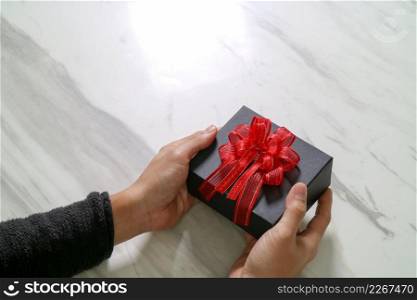 gift giving,man hand holding a gift box in a gesture of giving on white gray marble table background