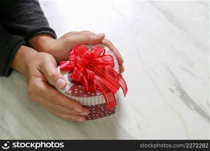 gift giving,man hand holding a heart shape gift box in a gesture of giving on white gray marble table background