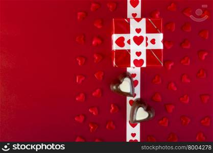 Gift with white ribbon and chocolate and red heart on red background. Valentine&rsquo;s day. Focus on gift box.