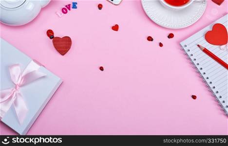 gift wrapped in a package on a pink background, on the side a white cup of tea with berries of a viburnum and an open notebook in a line