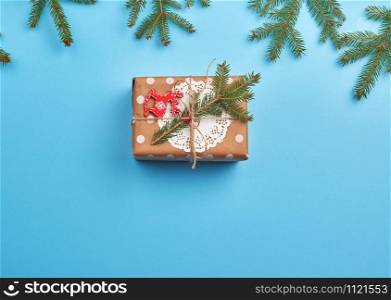 gift wrapped in brown craft paper and tied with a brown rope, decor from a green spruce branch on a blue background, top view