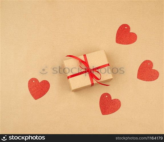 gift wrapped in brown kraft paper and tied with a thin silk ribbon on a background of paper, top view. Congratulations on Valentine&rsquo;s Day February 14