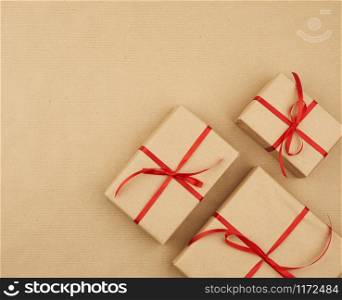 gift wrapped in brown kraft paper and tied with a thin silk ribbon on a background of paper, top view. Congratulations on Valentine&rsquo;s Day February 14