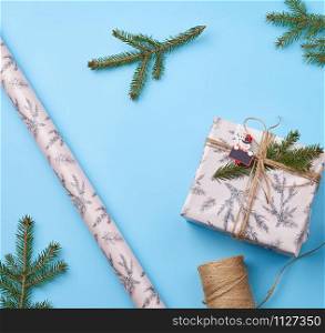 gift wrapped in pink paper and tied with a brown rope, decor from a green spruce branch on a blue background, top view