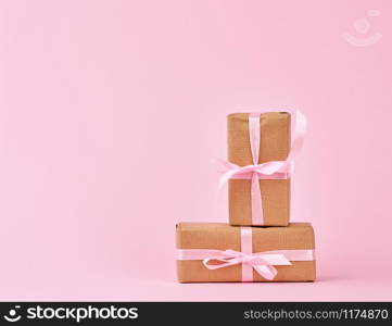 gifts in boxes wrapped in brown kraft paper and tied with pink silk ribbon on a pink background. Festive concept, copy space