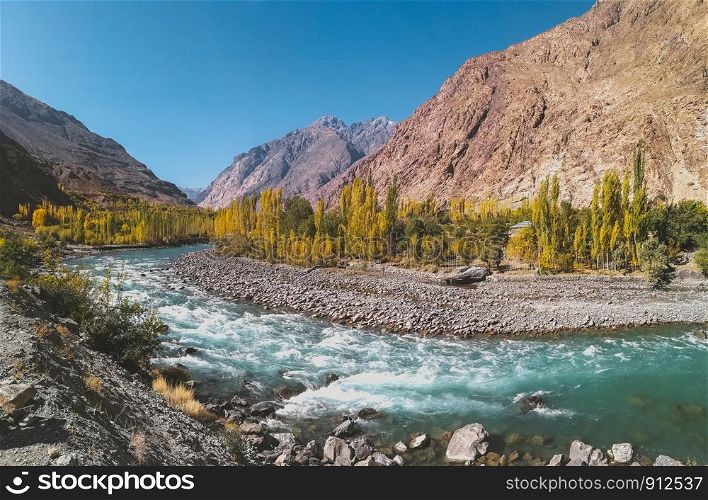 Gilgit river flowing through Gupis, with a view of Hindu Kush mountain range and trees in autumn. Ghizer, Gilgit Baltistan, Pakistan.