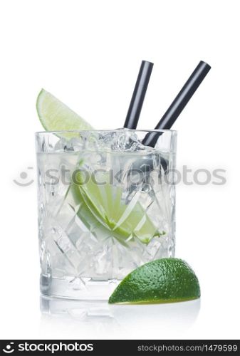 Gimlet cocktail in crystal glass with ice cubes and straw and lime slices on white background with lime on the side.