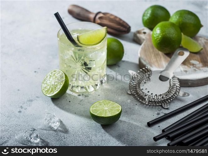 Gimlet Kamikaze cocktail in crystal glass with lime slice and ice on light background with fresh limes and strainer. Top view