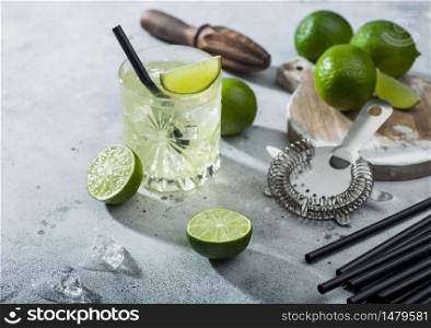 Gimlet Kamikaze cocktail in crystal glass with lime slice and ice on light background with fresh limes and strainer. Top view