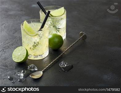 Gimlet Kamikaze cocktail in crystal glasses with lime slice and ice on black background with fresh limes and spoon. Top view
