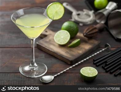 Gimlet Kamikaze cocktail in martini glass with lime slice and ice on wooden background with fresh limes and strainer with shaker. Top view