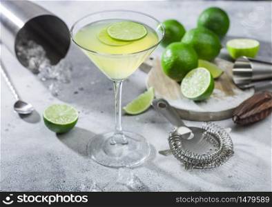 Gimlet Kamikaze cocktail in martini glass with lime slice and ice on light background with fresh limes and strainer with shaker. Coktail spoon and jigger.Top view
