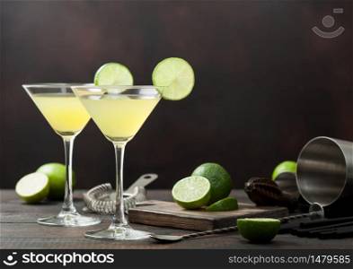 Gimlet Kamikaze cocktail in martini glasses with lime slice and ice on wooden background with fresh limes and strainer with shaker. Top view