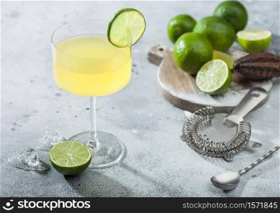 Gimlet Kamikaze cocktail in modern glass with lime slice and ice on light background with fresh limes and strainer with shaker.