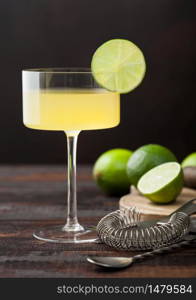 Gimlet Kamikaze cocktail in modern glass with lime slice wooden background with fresh limes and strainer.