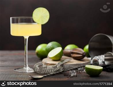 Gimlet Kamikaze cocktail in modern glass with lime slice wooden background with fresh limes and strainer with shaker.