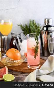 Gin cocktail with rosemary and pomegranate on a table among citrus fruits and drinks.