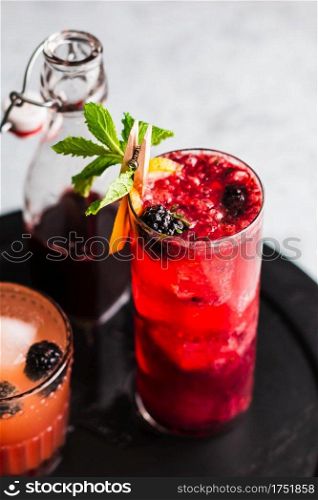 Gin in cocktail garnished with blackberries, lemon slice, and mint.