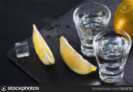 Gin or vodka in glasses with lemon wedges and ice on black background. Alcohol cocktail with citrus and herbs. Copy space