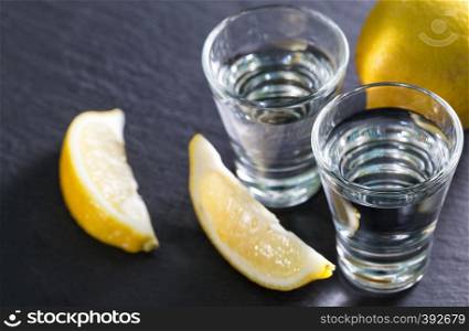 Gin or vodka in glasses with lemon wedges on a black background. Alcohol cocktail with citrus and herbs. Copy space