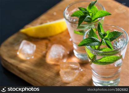 Gin or vodka with mint and lemon with ice on a wooden background. Alcoholic cocktail. Copy space. Toning. Gin or vodka with mint and lemon with ice