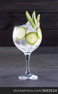 Gin tonic cocktail with cucumber and ice on black background