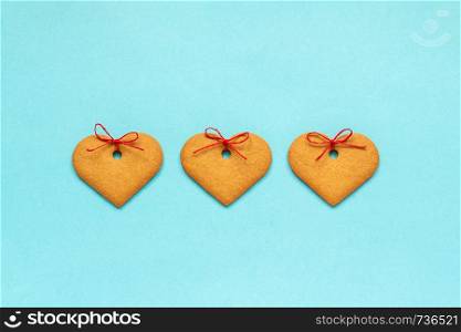 Ginger cookies heart-shaped decorated with a bow arranged in a row on a blue background. Top view Copy space Valentine card.. Ginger cookies heart-shaped decorated with a bow on blue background. Top view Copy space Valentine card