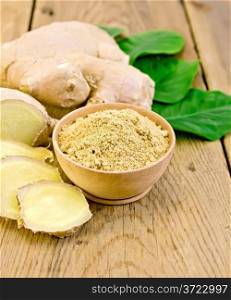 Ginger powder in a bowl, ginger root, green leaves on the background of wooden board