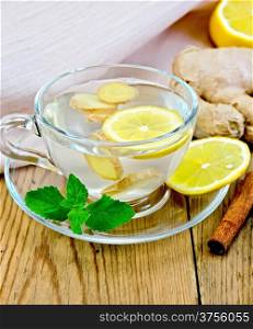 Ginger tea with lemon in a glass mug, mint, cinnamon, ginger root on the background of wooden boards