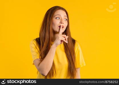 Ginger woman holding finger on lips, yellow studio background. Pretty lady with gesture of shhh, secret, silence, conspiracy, gossip concept. High quality photo. Ginger woman holding finger on lips, yellow studio background. Pretty lady with gesture of shhh, secret, silence, conspiracy, gossip concept