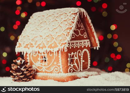 gingerbread house over defocused lights of Chrismtas decorated fir tree. The gingerbread house