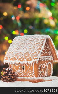 gingerbread house over defocused lights of Chrismtas decorated fir tree. The gingerbread house