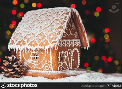 gingerbread house over defocused lights of Chrismtas decorated fir tree. The gingerbread house
