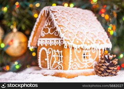 gingerbread house over defocused lights of Christmas decorated fir tree