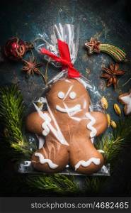 Gingerbread Man Cookie wrapped in Cellophane Bag and tied with Festive Ribbon on vintage background with fir branches and holiday decoration, top view, close up