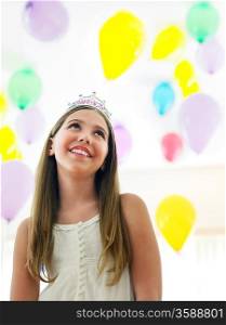 Girl (10-12) in tiara smiling looking up at balloons