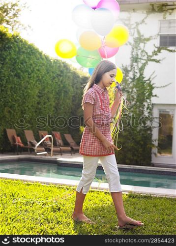 Girl (10-12) walking with balloons by swimming pool