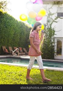 Girl (10-12) walking with balloons by swimming pool